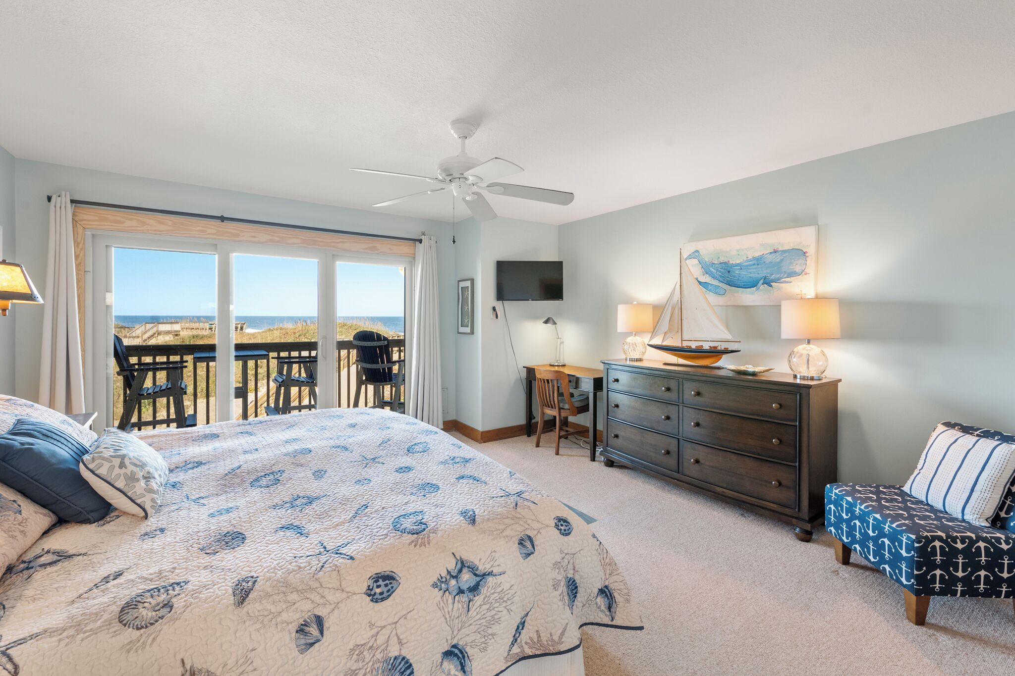 Ein Schlafzimmer mit einem großen Bett, einem Schreibtisch, einer Kommode und einem Balkon mit Blick auf das Meer.