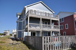 A multi-story building with a balcony on the second floor, a fenced yard, and a pool in the background.