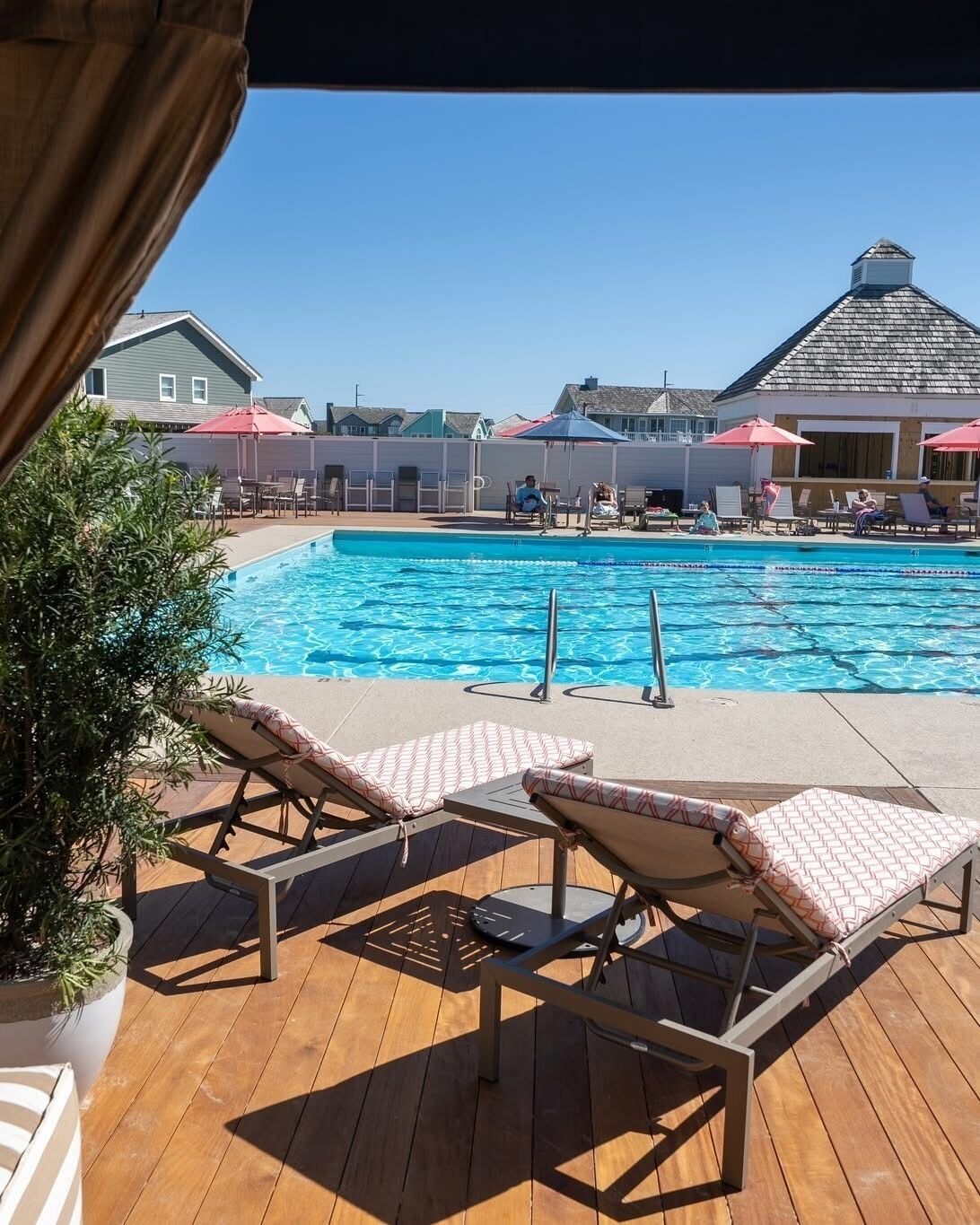A pool area with lounge chairs, a clear blue pool, and a view of houses in the background.