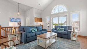 Ein geräumiges Wohnzimmer mit zwei blauen Sofas, einem Holztisch und einem großen Fenster mit Blick auf die Nachbarschaft.