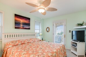 Une chambre à coucher avec un lit, un ventilateur de plafond, un tableau, une télévision et une porte donnant sur une vue agréable.
