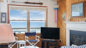 Un salon chaleureux avec une grande fenêtre donnant sur la mer, un téléviseur et une cheminée.