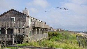 Un bâtiment en bois doté d’un balcon, situé près d’une plage, avec une clôture en bois et un ciel dégagé.