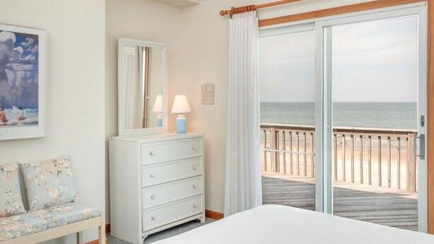 Une chambre d’hôtel avec un lit, une commode, un banc, un miroir et une vue sur la plage.