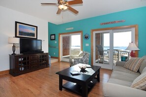 Relax in this inviting living room with a sofa, flat-screen TV, and sliding glass door leading to a scenic outdoor area.