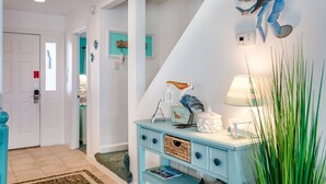 A hallway with a teal console table, a lamp, and a wall-mounted sculpture. - Oates Bluff: Pet friendly, Beach Club Access w/ Community Pool & Tennis Courts (Nags Head)
