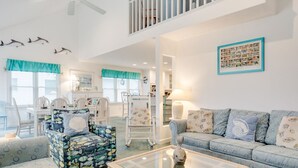A spacious living room with a high ceiling, a glass coffee table, a blue sofa, and patterned armchairs. - Oates Bluff: Pet friendly, Beach Club Access w/ Community Pool & Tennis Courts (Nags Head)