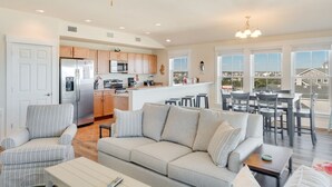 Una cocina moderna con refrigerador, microondas y estufa, un comedor con mesa y sillas, y una sala de estar con sofá y sillones.