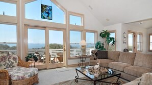 Amplia sala de estar con ventanas grandes, un sofá de mimbre, una mesa de centro de vidrio y vistas al mar.