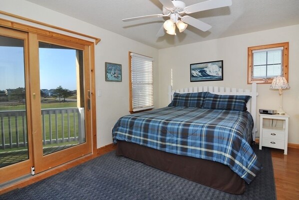 A bedroom with a bed, a ceiling fan, a nightstand, a lamp, and a view of the outdoors through a sliding door.