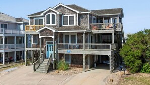 A two-story house with a balcony on the second floor, a front porch, and a staircase leading to the entrance. - Sandy Sea Gulls: Private Hot Tub, Short walk to Beach & Community Pool (Nags Head)
