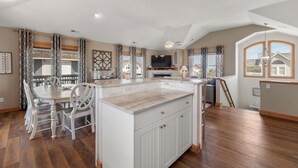 A spacious kitchen with a large island, dining area, and a TV. - Sandy Sea Gulls: Private Hot Tub, Short walk to Beach & Community Pool (Nags Head)