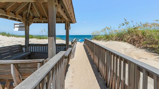 A wooden boardwalk leading to a beach with a wooden structure on the left. - Trip's OBX: Oceanfront Townhome, Pool, Tennis (Nags Head)