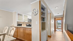 A modern kitchen with wooden cabinets, a microwave, and a dining area with wicker chairs. - Trip's OBX: Oceanfront Townhome, Pool, Tennis (Nags Head)