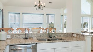 A kitchen with a granite countertop, stainless steel sink, and a dishwasher. There are wooden chairs and a chandelier. - Links End: Soundfront, Hot tub, Shared pool, Golf (Nags Head)