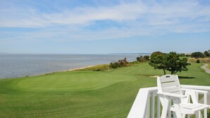 A golf course with a view of the ocean, a white chair, and a tree. - Links End: Soundfront, Hot tub, Shared pool, Golf (Nags Head)
