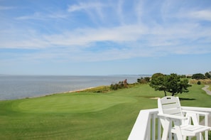 A golf course with a view of the ocean, a white chair, and a tree. - Links End: Soundfront, Hot tub, Shared pool, Golf (Nags Head)