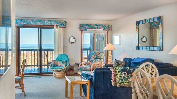 A living room with a view of the beach, a large window, and a dining area.