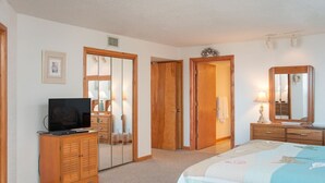 A bedroom with a bed, a TV on a wooden cabinet, a wardrobe, a mirror, and a door with a mirror.
