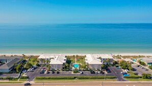 Un hotel costero con piscina central, varios estacionamientos y vista al mar.