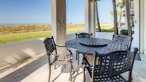 Un patio techado al aire libre con mesa y sillas, con vista a una playa.
