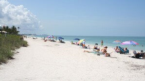A sandy beach with people relaxing under colorful umbrellas, a clear sky, and a calm sea. - Luxurious Mediterranean Style Home! The finest finishes - Private Heated Pool (ESTERO)