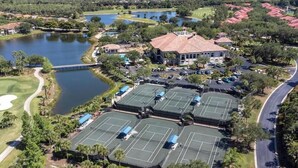 An aerial view of a residential area with multiple tennis courts, a large building with a red roof, and a lake. - Luxurious Mediterranean Style Home! The finest finishes - Private Heated Pool (ESTERO)