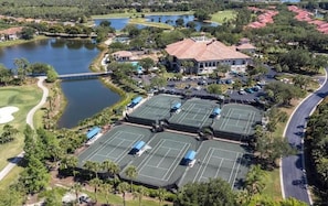 An aerial view of a residential area with multiple tennis courts, a large building with a red roof, and a lake.