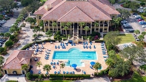 A large hotel with a central swimming pool, multiple balconies, and a parking area.