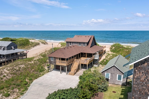 A coastal property with a large house featuring a deck and a staircase leading to a second floor.