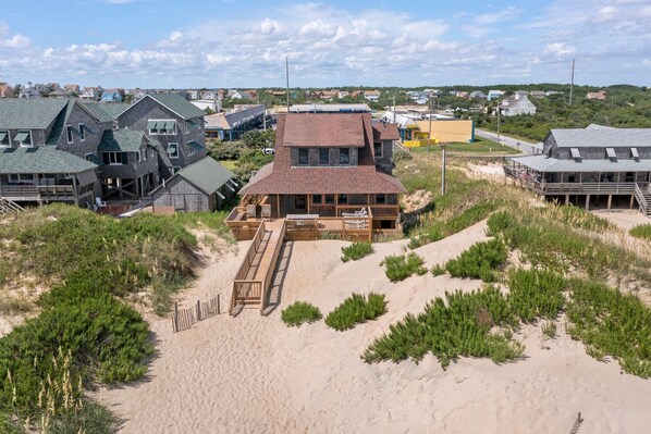 A beachfront property with a wooden deck, a sandy beach, and a view of the ocean.