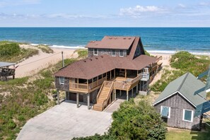 A beachfront property with a main house and a smaller cabin, featuring a covered deck and a staircase leading to the main house.