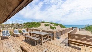 Una terraza de madera con bancos y mesas que da a una playa.