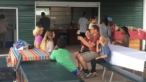 Un encuentro al aire libre con gente sentada en mesas, algunos de pie, y una zona de servicio de alimentos al fondo.