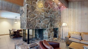 Una chimenea de piedra con fuego, un sofá de cuero y un comedor con sillas y una mesa.