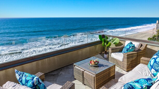 A seaside patio with wicker furniture, a table with fruit, and a view of the ocean.