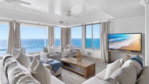 A spacious living room with a large TV, comfortable seating, and a view of the ocean.