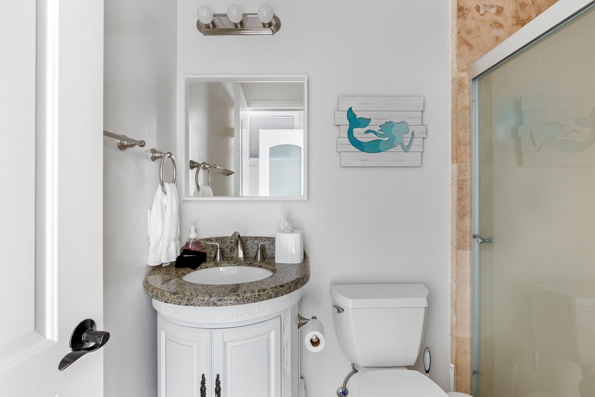 A bathroom with a granite countertop sink, a white toilet, a mirror above the sink, and a towel hanging on a towel rack.