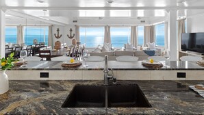 A spacious living area with a large window overlooking the sea, a dining area with a view, and a kitchen with a modern sink.