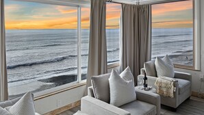 A room with a large window overlooking the ocean, featuring a sofa and a small table with a book and a bottle.