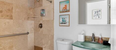 Een badkamer met een glazen wastafel, toilet en douchegedeelte. Twee ingelijste foto's hangen aan de muur.