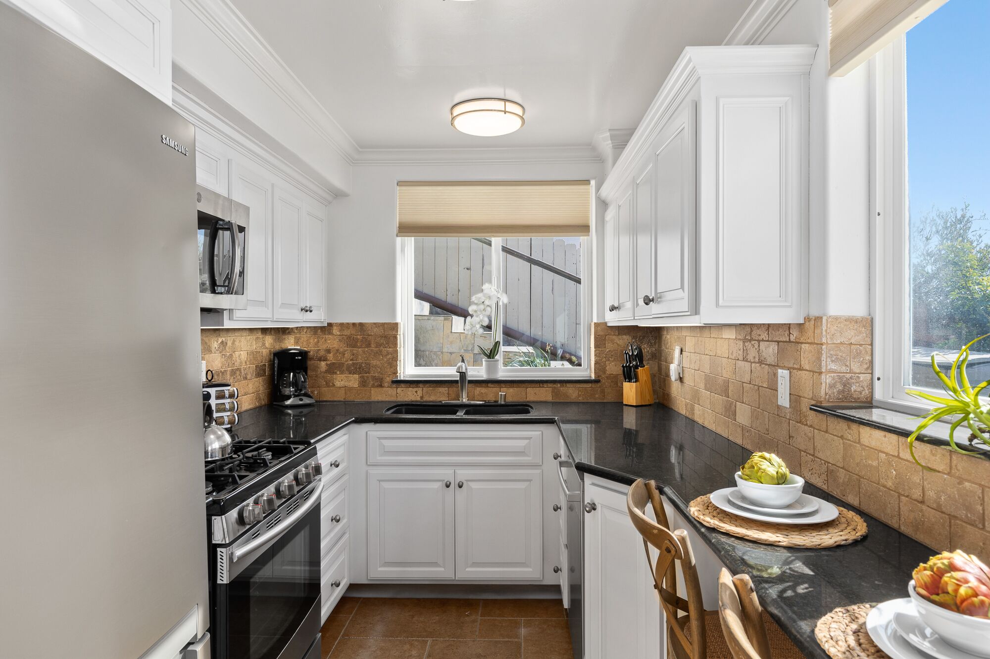 A kitchen with white cabinets, a black countertop, a built-in stove, and a window with a view of a wooden deck.