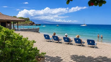 Ein Strand mit Liegestühlen, einem Pool und Booten im Wasser.