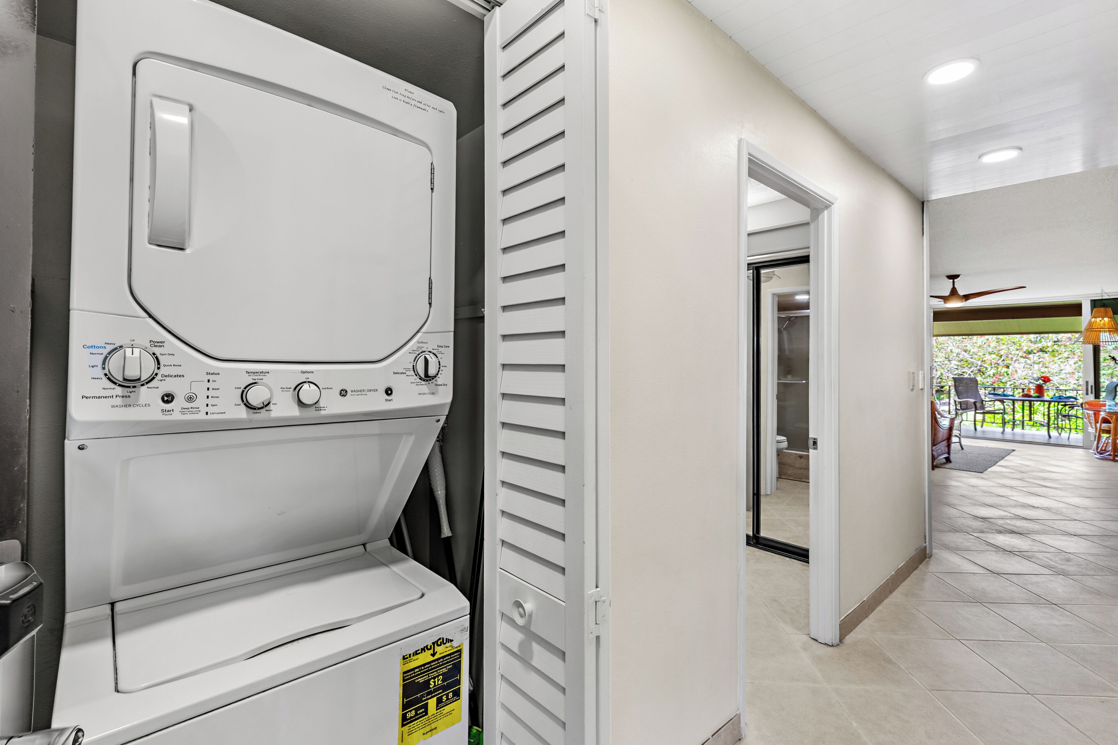 A laundry area with a front-loading washer and dryer, a door leading to a balcony, and a tiled floor.