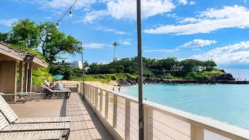 Eine Holzterrasse mit Liegestühlen, einem Geländer und Blick aufs Meer.