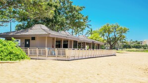 Ein Gebäude direkt am Strand mit einer überdachten Veranda, einem Sandstrand und Bäumen im Hintergrund.