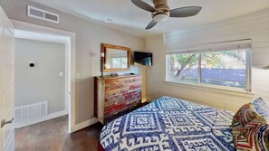 A bedroom with a bed, dresser, TV, and a window with a view.