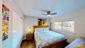 Un dormitorio con una cama de madera, ventilador de techo, ventana con vistas y una lámpara fijada a la pared.