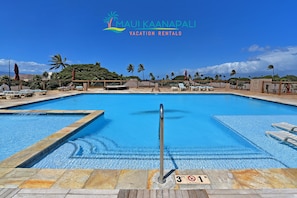 Relax by the pool with a central diving board and lounge chairs, surrounded by palm trees.