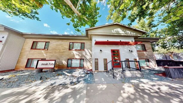 A two-story building with a red garage door, a sign reading 'moab flats,' and a gravel driveway.
